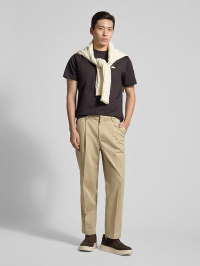 Männermodel trägt Regular Fit Chino aus Baumwoll-Mix Modell 'TAAMIR PLEATED' von Armedangels in Beige, unifarben, mit Logo-Stitching, Ganzkörperansicht von vorne.