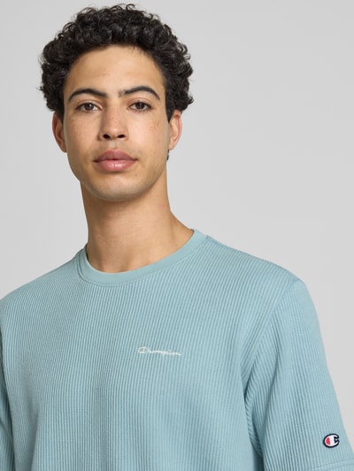 Männermodel trägt T-Shirt mit Strukturmuster und Label-Stitchings von CHAMPION in Hellblau aus Baumwoll-Mix, Regular-Fit, Nahaufnahme Oberkörper.