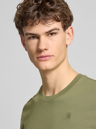 Mannenmodel draagt T-Shirt aus Baumwolle van G-Star Raw in olijfgroen, ronde hals, rechte fit, zachte textuur, label-stitching, close-up bovenlichaam.