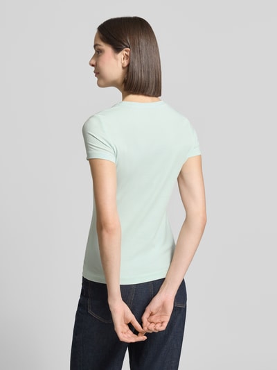 Frauenmodel trägt Slim Fit T-Shirt mit Strasssteinbesatz von Guess, helles Damen T-Shirt aus elastischem Baumwoll-Mix, Rückansicht Ganzkörperansicht.