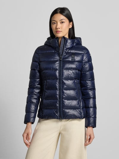 Frauenmodel trägt dunkelblaue Jacke in Stepp-Optik Modell 'CAROLL' von Blauer USA mit Logo und Kapuze, Ganzkörperansicht von vorne.