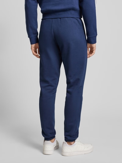 Mannelijk model draagt 'Sweatpants mit elastischem Bund' van adidas Originals in donkerblauw katoenmix, losvallende pasvorm, gestikte labeldetails, Franse steekzakken, elastische tailleband, volledige lichaamsopname achterkant.