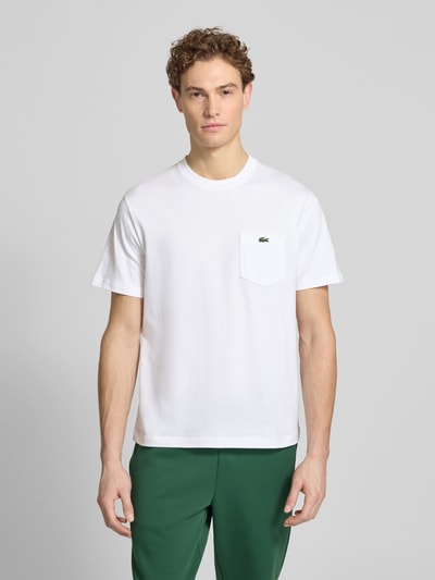 Männermodel trägt Regular Fit T-Shirt aus reiner Baumwolle von Lacoste in Weiß mit Logo-Stitching, unifarben, Rundhals; Ganzkörperansicht von vorne.