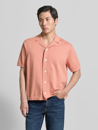 Männermodel trägt Regular Fit Strickjacke aus reiner Baumwolle Modell 'AMOUR' von SELECTED HOMME in Optik: Unifarben, einreihige Knopfleiste, Intarsie, Reverskragen, Kurzarm, Materialverarbeitung: Strick, Farbe Pfirsich, glatte Textur, Ganzkörperansicht von vorne.