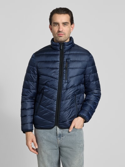 Męski model nosi Regular Fit Steppjacke mit Stehkragen od Tom Tailor, granatowy kolor, steppowana faktura, wodoodporna, zapinana na zamek, z bocznymi i piersiową kieszenią, elastyczne wykończenia, label patch i kontrastowe detale, ochrona przed zimnem, Ganzkörperansicht von vorne.