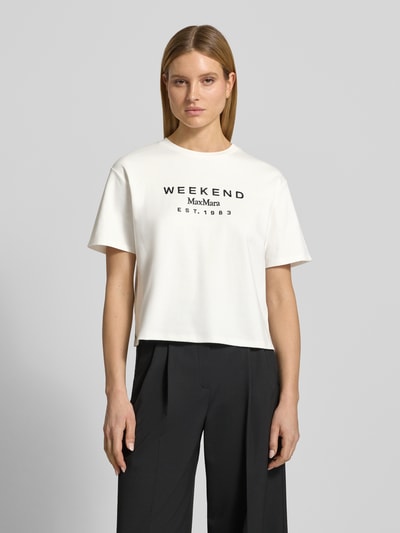 Kobiece modelka nosi damski t-shirt Regular Fit T-Shirt aus reiner Baumwolle Modell 'SABATO' od Weekend Max Mara, efekt: jednolity kolor, krój regular fit, wyhaftowana aplikacja kwiatowa, okrągły dekolt, rękaw: krótki rękaw, wykończenie materiału: drobne prążkowanie, materiał: czysta bawełna; widok na górną część ciała z przodu.