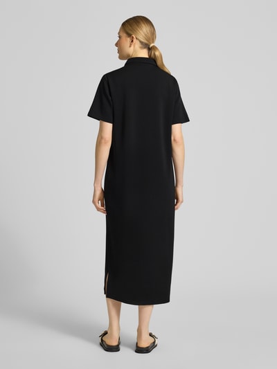 Frauenmodel trägt schwarzes Polokleid mit Knopfleiste Modell 'Helle' von My Essential Wardrobe, gerader Schnitt, Midikleid, Material-Mix, Ganzkörperansicht Rückansicht.
