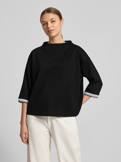Frauenmodel trägt Relaxed Fit Pullover mit Viskose-Anteil Modell 'Utalba' von Someday in Schwarz mit Stehkragen, Halbarm, Elastischer Material-Mix, Ganzkörperansicht von vorne.