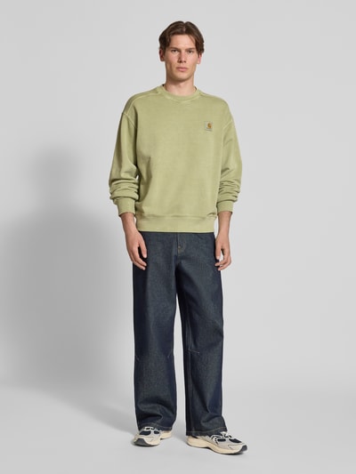 Männermodel trägt Sweatshirt mit Label-Detail Modell 'Nelson' von Carhartt Work In Progress in Grün aus Reine Baumwolle, Relaxed-Fit, Ganzkörperansicht von vorne. Rückenlänge 68 cm, Ärmellänge 63 cm.