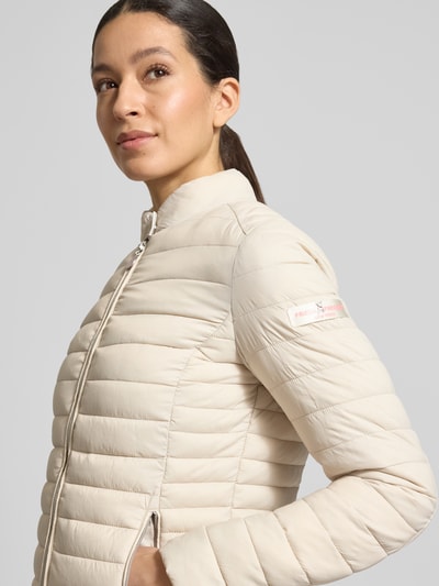 Vrouwenmodel draagt gewatteerd jack model 'JUDY' van Frieda & Freddies in creme, slim fit, opstaande kraag, tweewegritssluiting, ritsszakken, ruglengte maat 36: 57 cm, schouderbreedte: 40 cm, borstwijdte: 48 cm, mouwlengte: 64 cm, detailopname bovenlichaam.