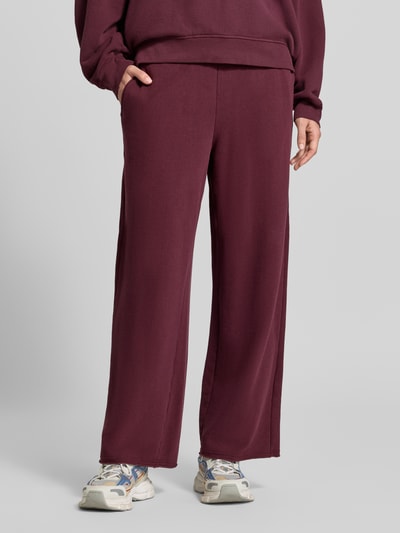 Frauenmodel trägt Straight Fit Sweatpants aus elastischem Baumwoll-Mix von American Vintage in Dunkelrot, Nahaufnahme Unterkörper. Damen Sweatpants, elastisches Material, Modell 'ATUBAY', Bund mit Tunnelzug, Innenbeinlänge 72 cm bei Größe S.