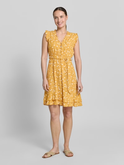 Frauenmodel trägt Minikleid aus Viskose mit Bindegürtel und Kappärmeln von Apricot in Gelb mit weißen Punkten, Taillierter Schnitt, V-Ausschnitt mit Rüschen, kurze Knopfleiste, Stufenrock, Rückenlänge 89 cm, Brustweite 38 cm, Ganzkörperansicht von vorne.