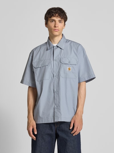 Männermodel trägt Relaxed Fit Freizeithemd mit Kentkragen und Label-Detail von Carhartt Work In Progress, Material-Mix, Brusttaschen, Ganzkörperansicht von vorne. Rückenlänge bei Größe M: 75 cm, Schulterbreite: 51 cm, Ärmellänge: 28 cm.