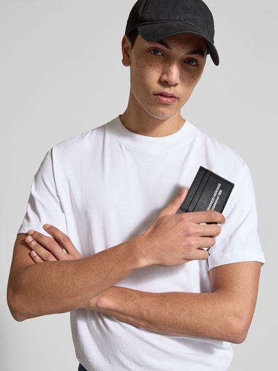 Männermodel trägt Portemonnaie mit Label-Detail von Dsquared2 aus schwarzem, beschichtetem Leder, Steckfächer, Nahaufnahme Oberkörper.