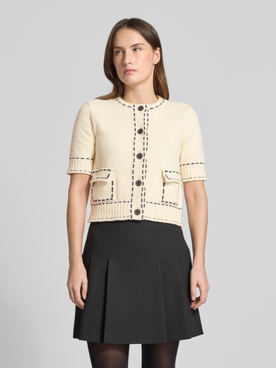 Modelka kobieca nosi Slim Fit Strickjacke mit aufgesetzten Taschen od Rich & Royal, kremowy bawełniany miks, kontrastowe szwy, półrękaw, okrągły dekolt, kieszenie naszywane, krój slim fit, zapięcie na guziki, elastyczne wykończenia, długość tyłu 42 cm, długość rękawa 26 cm, widok całej sylwetki z przodu.