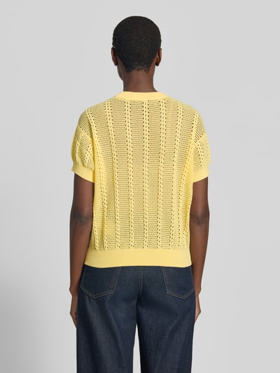 Frauenmodel trägt Relaxed Fit Strickshirt aus Baumwoll-Mix Modell 'LUX LIGHT' von Vero Moda in Optik: Unifarben mit Lochstrickmuster, kurze Ärmel, Rundhals, Ärmelabschluss und Rumpfabschluss gerippt, Farbe hellgelb, Materialverarbeitung: Lochstrick, Ganzkörperansicht Rückansicht.