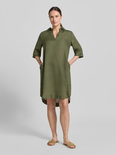 Frauenmodel trägt knielanges Damen Leinenkleid Modell 'DERRY' von 0039 Italy in Olivgrün, gerader Schnitt, Hemdblusenkragen, V-Ausschnitt, Seitentaschen, glatte Textur, Ganzkörperansicht von vorne.