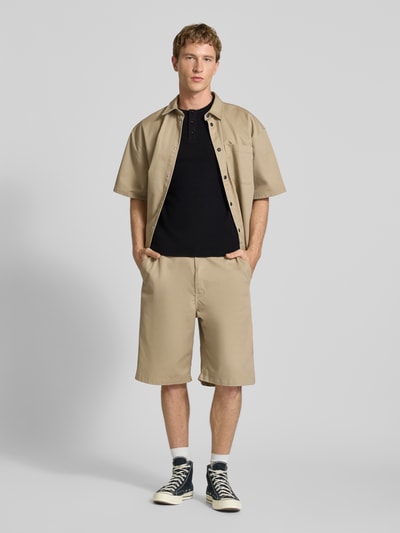 Männermodel trägt T-Shirt mit kurzer Knopfleiste von REVIEW in Schwarz, Baumwoll-Mix mit Stretch-Anteil, Körpernaher-Schnitt, Feinripp, Rundhalsausschnitt, Rückenlänge bei Größe M 64 cm, Ganzkörperansicht von vorne.