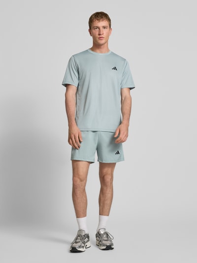 Männermodel trägt T-Shirt mit Logo und Rundhalsausschnitt von adidas Training in Hellblau, Regular Fit, glatte Textur, Ganzkörperansicht von vorne.