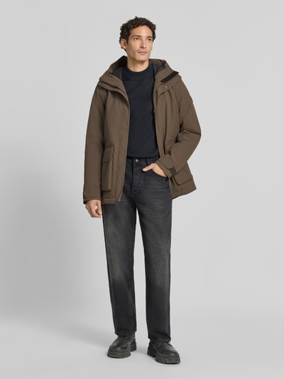 Männermodel trägt Regular Fit Jacke mit aufgesetzten Taschen Modell 'Liam' von Didriksons in Braun, Kapuze, schwarze Hose, Ganzkörperansicht von vorne. Herren Jacke, Rückenlänge 79 cm, Schulterbreite 44 cm, Brustweite 45 cm, Ärmellänge 70 cm.