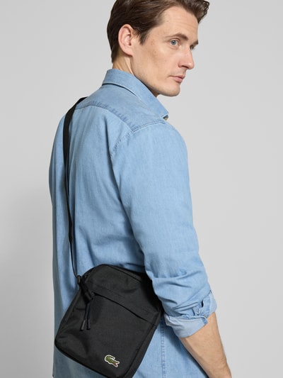 Männermodel trägt Umhängetasche mit von Lacoste, unifarben, rechteckig, Label Patch, Ganzkörperansicht Rückansicht