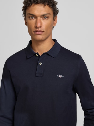 Męskimodel nosi Regular Fit Koszulka polo z wyhaftowanym logo marki Gant, 100% bawełna, kołnierzyk polo, listwa guzikowa, kolor granatowy, długość tyłu 68 cm w rozmiarze M, ujęcie: z przodu, zbliżenie na górną część ciała.