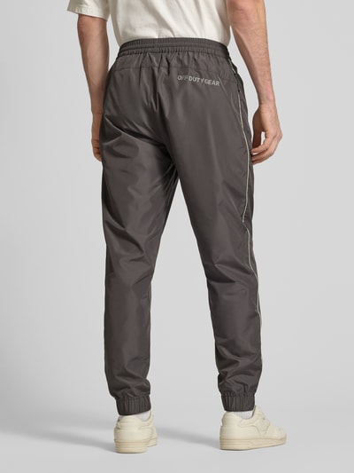 Männermodel trägt Trainingshose mit elastischem Bund von HALO in Dunkelgrau mit Label-Print, Relaxed Fit, Reißverschlusstaschen, Ganzkörperansicht Rückansicht. Innenbeinlänge bei Größe M: 40 cm.
