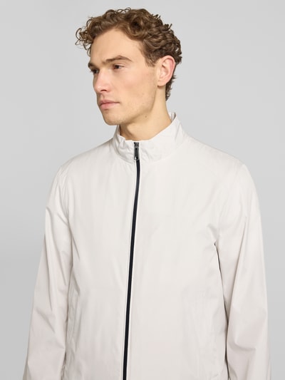 Męski model nosi Blouson mit Stehkragen und Reißverschluss od Geox, jasny kolor, krój regular fit, stójka, zamek błyskawiczny, wpuszczane kieszenie, długość tyłu w rozmiarze M: 68 cm, szerokość ramion w rozmiarze M: 46 cm, szerokość klatki piersiowej w rozmiarze M: 56 cm, długość rękawów w rozmiarze M: 68 cm, z przodu, zbliżenie na górną część ciała