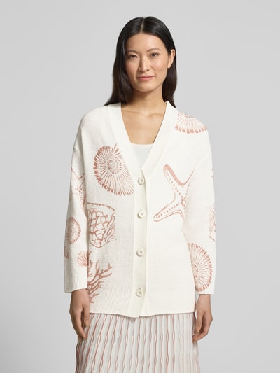 Modelka nosi Cardigan mit V-Ausschnitt im Allover-Look von Marc Cain, bawełniany miks, krój relaxed fit, wzór allover, dekolt w serek, listwa guzikowa, długość pleców w rozmiarze 36: 70 cm, długość rękawa w rozmiarze 36: 56 cm, kremowe i beżowe odcienie, prosta faktura, wzory muszli i rozgwiazd, widok całej sylwetki z przodu.