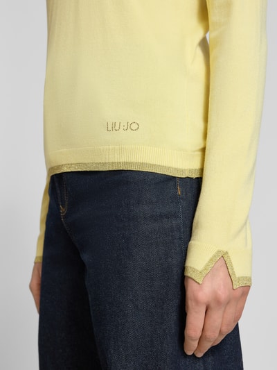 Frauenmodel trägt Slim Fit Longsleeve aus Viskose-Mix mit V-Ausschnitt von Liu Jo White, dezentes Logo-Detail, elastische Abschlüsse, gelb, fein strukturierte Textur, Longsleeve endet bei Größe S auf 55 cm Rückenlänge, Ärmel 58 cm, Nahaufnahme Oberkörper.