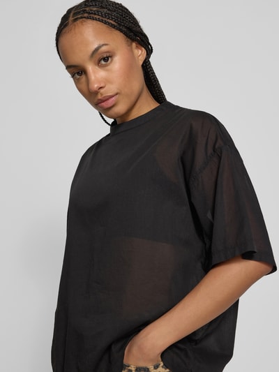 Frauenmodel trägt T-Shirt in semitransparenter Optik von black palms aus reiner Baumwolle im lockeren Schnitt, Nahaufnahme Oberkörper.