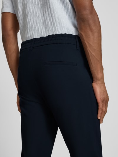 Męski model nosi Hose mit Eingrifftaschen Modell 'CHASY' od Drykorn, krój tapered fit, elastyczny pas, lejkowate kieszenie, tekstura gładka, materiał z domieszką wiskozy, widok na tył, ujęcie detaliczne