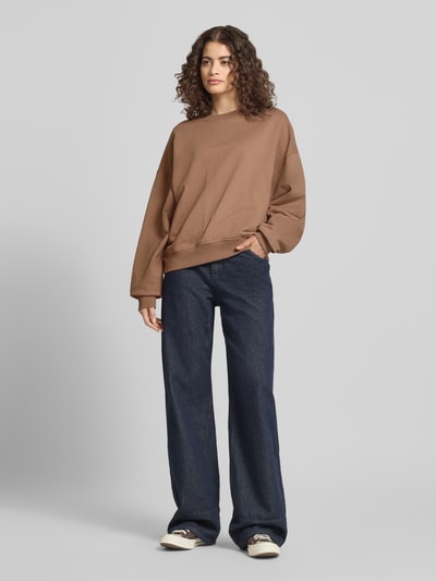 Frauenmodel trägt Regular Fit Sweater mit Logo-Stitching Modell 'Croissant' von OH APRIL in Braun, Baumwolle, weite Jeans, Ganzkörperansicht von vorne