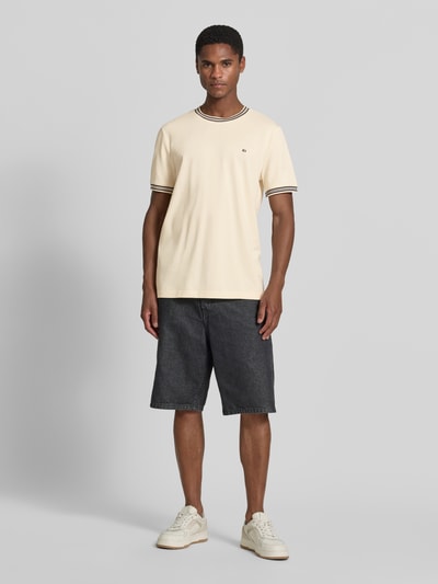 Męski model nosi Regular Fit T-Shirt mit Logo-Stitching od Christian Berg Men, kremowy, czarny detal, czysta bawełna, krój regular fit, dekolt okrągły, długość tyłu w rozmiarze M: 71 cm, pełny widok z przodu.