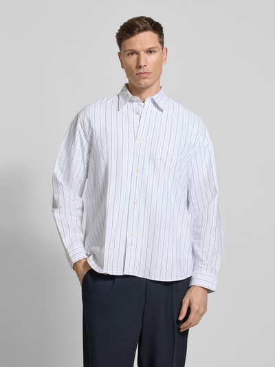 Männermodel trägt weißes Relaxed Fit Freizeithemd aus reiner Baumwolle Modell 'OXFORD SHIRT' von Selected Homme mit Allover-Muster, gestreift, Kentkragen, durchgehender Knopfleiste, Brusttasche und 1-Knopf-Manschette, Ganzkörperansicht von vorne.