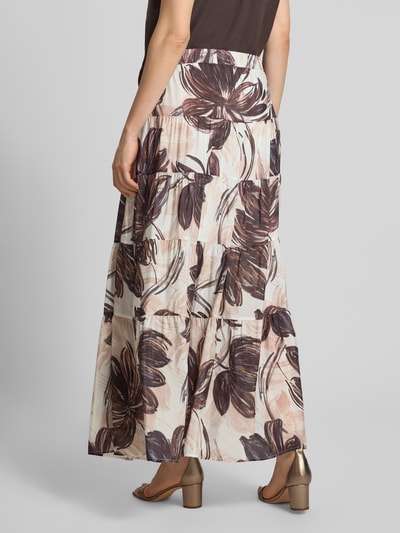 Vrouwenmodel draagt maxirok uit mix van viscose en katoen met A-lijn, elastische band, all-over bloemenprint van MORE & MORE, totale lengte maat 36: 100 cm, bandwijdte maat 36: 44 cm, bloemenmotief in bruin en crème, geheel bedekt, textuur licht en vloeiend, volledige achteraanzicht