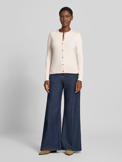 Vrouwenmodel draagt Regular Fit gebreid jack uit viscosemix met geschulpte zoom van Christian Berg Woman, ivoor, lange mouw, blauwe wijde jeans, knoopsluiting, ribboorden, ruglengte maat S 56 cm, mouwlengte 61 cm, volledig lichaam vooraanzicht.