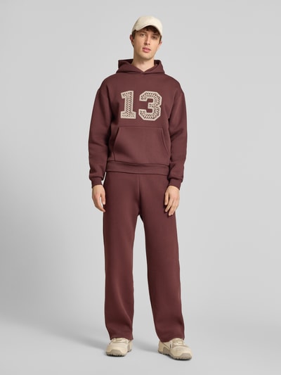 Männermodel trägt Hoodie mit Ketten-Stickerei und Känguru-Tasche von REVIEW in Braun, Baumwoll-Mix, Regular-Fit, Ganzkörperansicht von vorne.