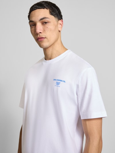 Męski model nosi Relaxed Fit T-Shirt aus reiner Bio-Baumwolle Modell 'FRED' od Only & Sons, biała gładka tkanina, nadruk z przodu, krótki rękaw, okrągły dekolt, czysta bio-bawełna, Ganzkörperansicht von vorne.