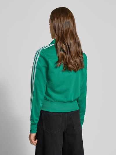 Kobiece modelka nosi zieloną „Trainingsjacke mit Label-Stitching” od adidas Originals, krój regular fit, widok całej sylwetki od tyłu.