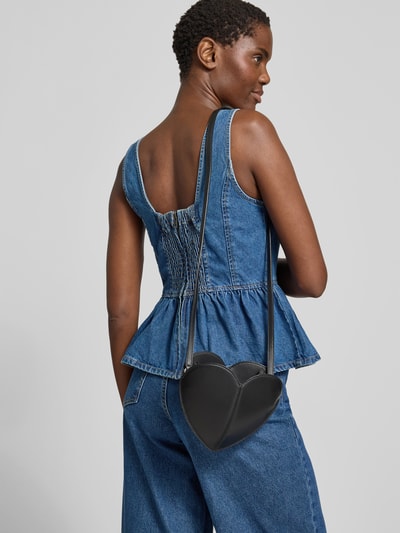 Frauenmodel trägt Crossbody Bag aus echtem Leder von ROTATE in Schwarz, herzförmig, mit Ziernaht und schmalem Schulterriemen; Ganzkörperansicht Rückansicht.