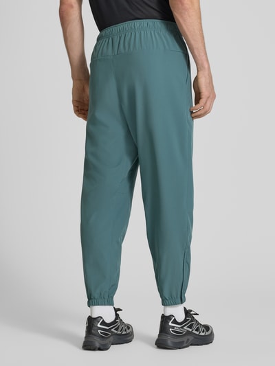 Männermodel trägt Form Pants mit Logo-Print und Eingrifftaschen von NIKE TRAINING in Petrol, Körpernaher-Schnitt, Ganzkörperansicht Rückansicht.