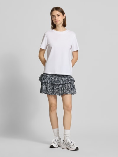 Frauenmodel trägt Ausgestellter Mini-Rock mit Volants Modell 'ZOEY' von Only, Optik: Florales-Allover-Muster, Regular-Fit, Mini-Länge, Volants, gesmokter Bundabschluss, Material: reine Baumwolle, dunkle und helle Farbtöne, weiche Textur, Ganzkörperansicht von vorne.