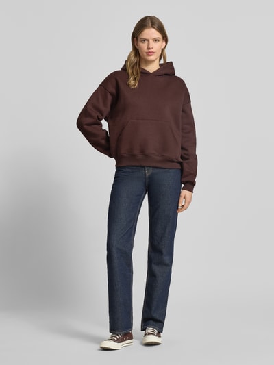 Frauenmodel trägt Regular Fit Hoodie mit Känguru-Tasche Modell 'Iconic' von Gina Tricot, mieszanka bawełny, krój regular fit, kieszeń kangurka, wykończenia: elastyczne. Ganzkörperansicht von vorne.