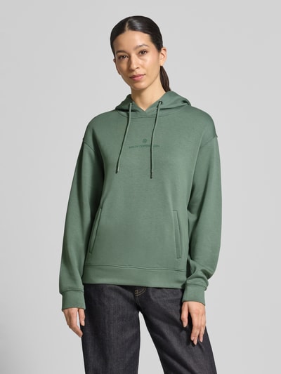 Modelka kobieca nosi zielony Hoodie z tunelem model 'IMA' od MSCH Copenhagen, prosto skrojony, widoczne kieszenie, widok z przodu, ujęcie całej sylwetki.