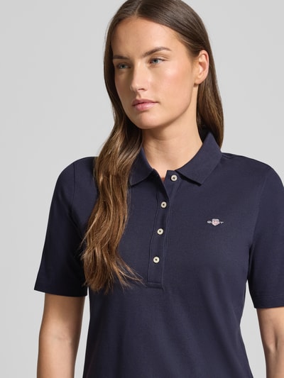 Frauenmodel trägt Poloshirt aus Baumwolle mit Label-Detail von GANT in Dunkelblau, gerader Schnitt, Polokragen, 1/2-Arm, Nahaufnahme Oberkörper.