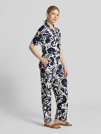 Vrouwenmodel draagt jumpsuit met florale all-over print van Oui in donkerblauw en crème, elastische materiaalmix, getailleerd, reverskraag, knoopsluiting, met korte mouwen, gladde structuur, dames jumpsuit, totale lengte maat 36: 146 cm, borstwijdte: 51 cm, binnenbeenlengte: 76 cm, geheellichaamsaanzicht van voren.