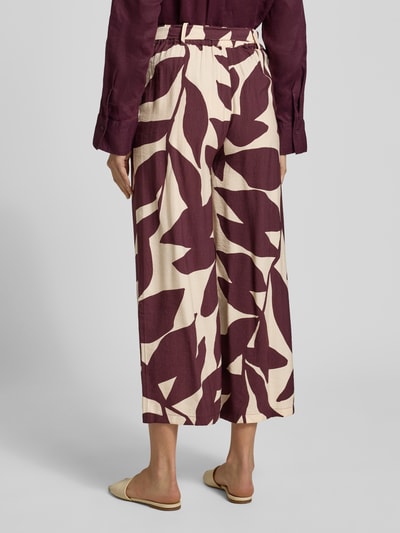 Frauenmodel trägt Stoffhose aus Viskose-Mix mit Bindegürtel Modell 'PLUMAS' von Mango, weinrote Blätter auf cremefarbenem Grund, Ganzkörperansicht Rückansicht. Relaxed Fit, verkürzte Passform, Allover-Look, Kontext: Damen Stoffhose, Bundweite S 36 cm, Innenbeinlänge S 67 cm.