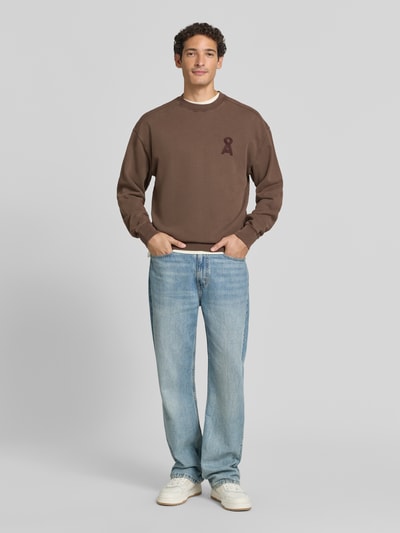 Männermodel trägt braunes Relaxed Fit Sweatshirt aus reiner Baumwolle Modell 'ICONIC Å' von ARMEDANGELS, helle Jeans, Ganzkörperansicht von vorne, Herren Sweatshirt