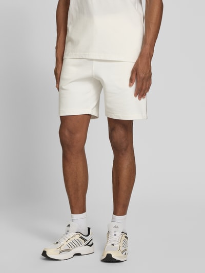Männermodel trägt Regular Fit Sweatshorts aus reiner Baumwolle von Lacoste in Unifarben, Logostreifen, elastischer Bund, Nahaufnahme Oberschenkel bis Füße.